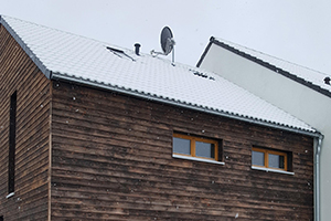 Ein mit Holz verkleidetes Strohballenhaus. Schnee liegt auf dem Dach.
