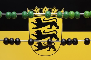 Grüne und schwarze Zählperlen sind vor der Flagge Baden-Württembergs zu sehen.